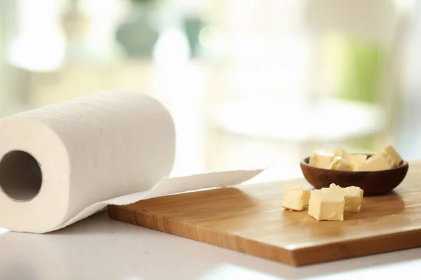 Roll of paper towels and wooden board with butter on kitchen table — Stock Photo, Image