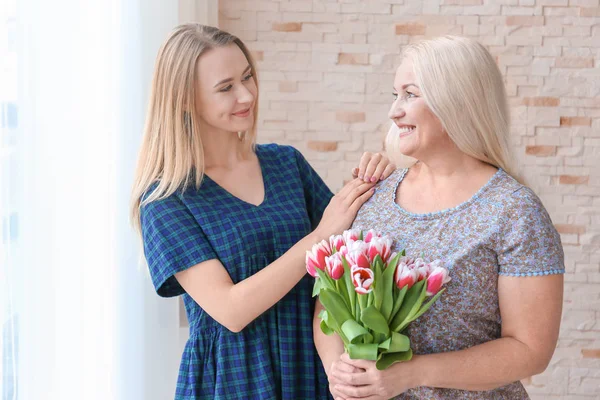 Young daughter and mother with bouquet of flowers at home — Stock Photo, Image