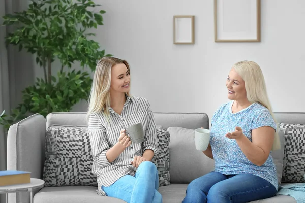 Unga dotter och mor dricka kaffe på soffan hemma — Stockfoto