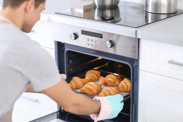 Uomo che prende la teglia con deliziosi croissant dal forno elettrico in cucina — Foto Stock