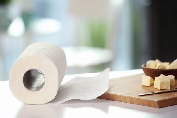 Roll of paper towels and wooden board with butter on kitchen table — Stock Photo, Image