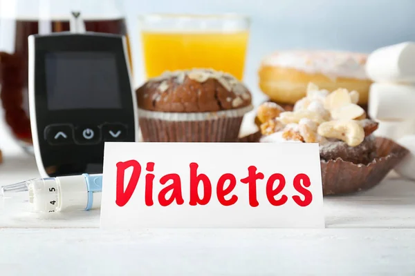 Card with word "Diabetes", sweets and digital glucometer on table — Stock Photo, Image
