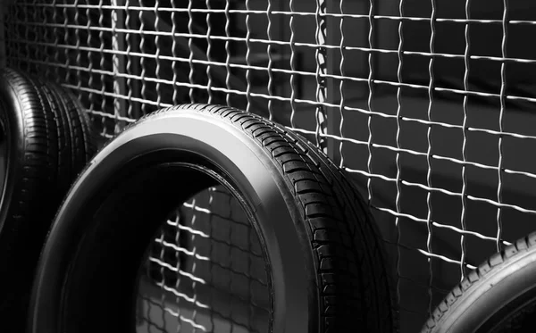 Neumático de coche cerca de valla de rejilla en interiores —  Fotos de Stock