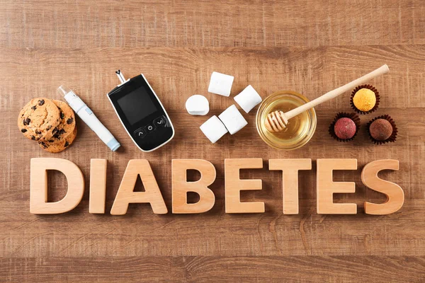 Состав со словом "диабет", сладости и цифровой глюкометр на деревянном фоне — стоковое фото