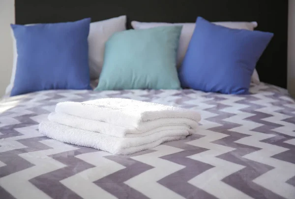 Comfortable bed with folded towels in room interior — Stock Photo, Image