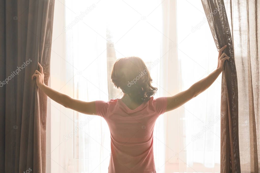 Young woman opening curtains indoors
