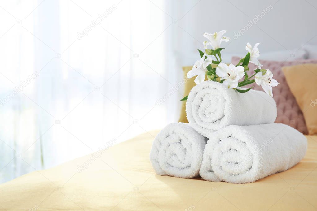Rolled white towels with flowers on bed