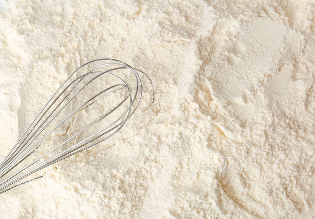 Metal whisk on white wheat flour