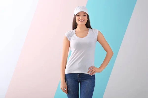 Jovem mulher em elegante t-shirt e boné sobre fundo de cor. Mockup para design — Fotografia de Stock
