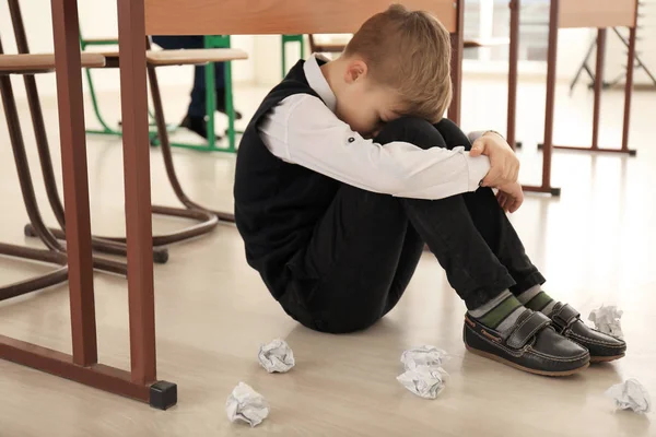 Upset little boy sitting on floor indoors. Bullying in school — Stock Photo, Image