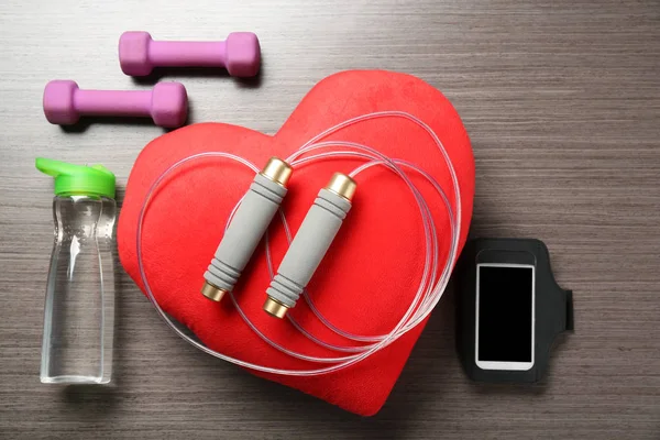 Cosas del gimnasio, teléfono y corazón rojo sobre fondo de madera. Concepto de entrenamiento cardiovascular —  Fotos de Stock