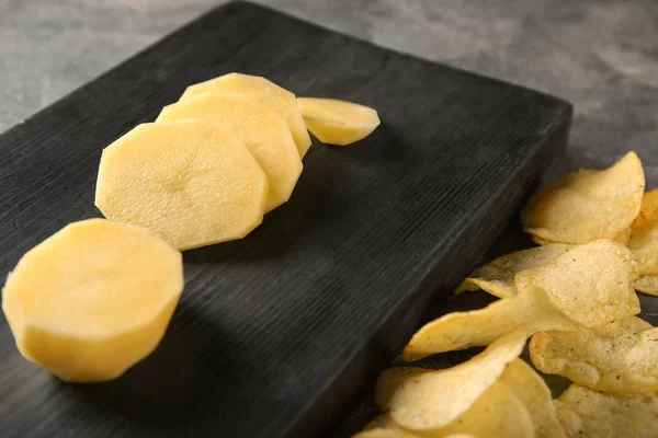 Crispy chips and raw potato on table — Stock Photo, Image