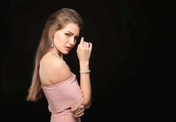 Schöne junge Frau mit elegantem Schmuck auf dunklem Hintergrund — Stockfoto