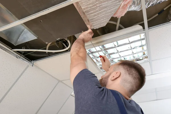 Técnico masculino reparando condicionador de ar industrial dentro de casa — Fotografia de Stock