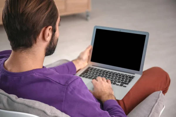 Człowiek z laptopa siedząc w wygodnym fotelu w domu — Zdjęcie stockowe