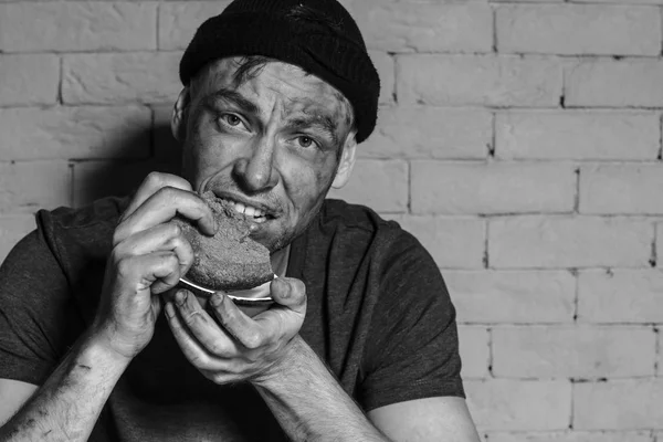 Fome pobre homem comendo pedaço de pão perto da parede de tijolo — Fotografia de Stock