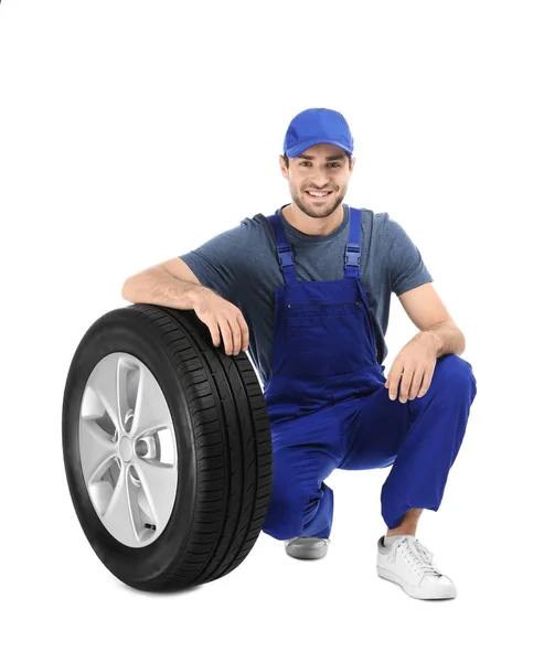 Jovem mecânico em uniforme com pneu de carro no fundo branco — Fotografia de Stock