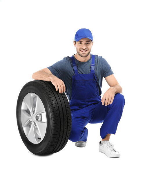 Young mechanic in uniform with car tire on white background