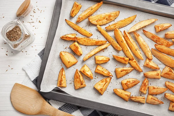 Hoja para hornear con deliciosas patatas horneadas al horno en la mesa —  Fotos de Stock