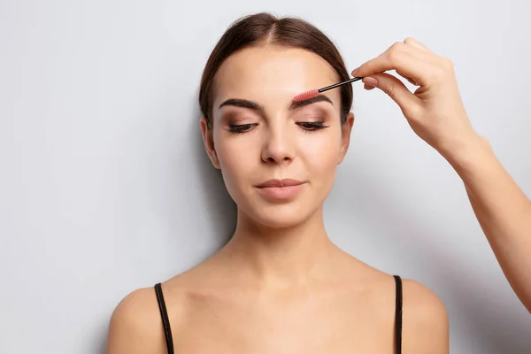 Ung kvinna genomgår ögonbrynskorrigering förfarande på ljus bakgrund — Stockfoto