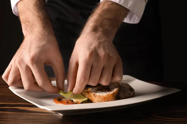 Männlicher Koch in Uniform bereitet schmackhaftes Gericht auf dem Tisch zu, Nahaufnahme — Stockfoto