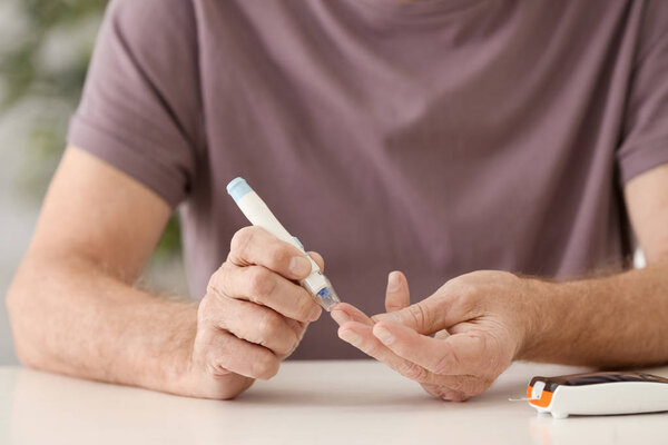 Elderly man with diabetes measuring level of blood sugar at home, closeup