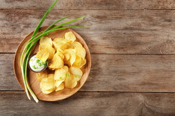 Krispig potatis chips med grön lök och gräddfil på träplatta, ovanifrån — Stockfoto