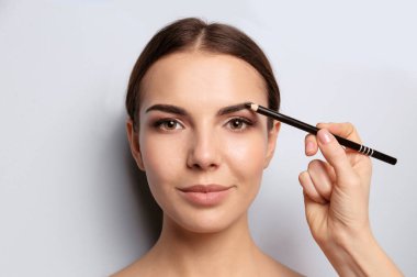 Young woman undergoing eyebrow correction procedure on light background clipart