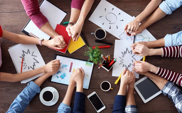 Jóvenes tomados de la mano mientras trabajan en el proyecto en la mesa. Concepto de unidad — Foto de Stock