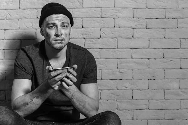 Hungry poor man holding bowl with piece of bread while sitting near brick wall — Stock Photo, Image