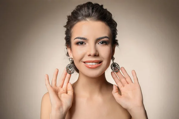 Schöne junge Frau mit elegantem Schmuck auf farbigem Hintergrund — Stockfoto