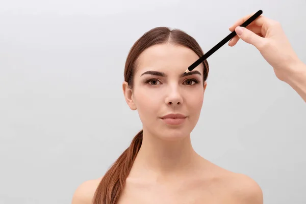 Young woman undergoing eyebrow correction procedure on light background — Stock Photo, Image