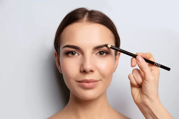 Young woman undergoing eyebrow correction procedure on light background — Stock Photo, Image