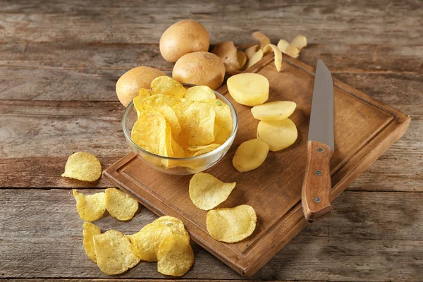 Cuenco con papas fritas crujientes y patatas crudas sobre mesa de madera —  Fotos de Stock