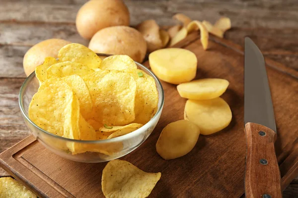 Cuenco con papas fritas crujientes y patatas crudas sobre mesa de madera —  Fotos de Stock