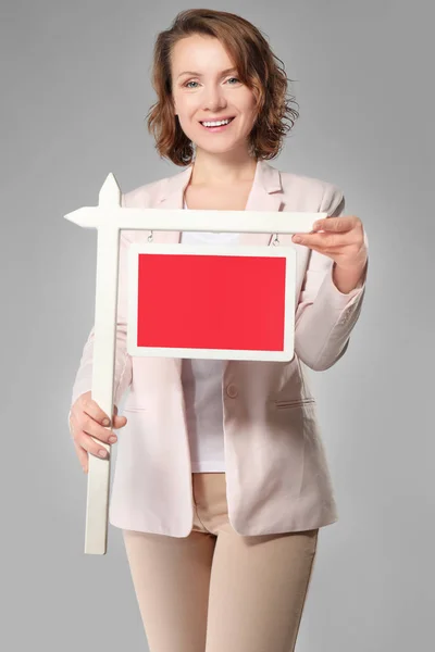 Agente inmobiliario con signo en blanco sobre fondo gris — Foto de Stock