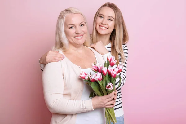 Hija y madre jóvenes con ramo de flores sobre fondo de color — Foto de Stock