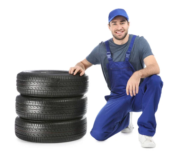 Joven mecánico en uniforme con neumáticos de coche sobre fondo blanco — Foto de Stock