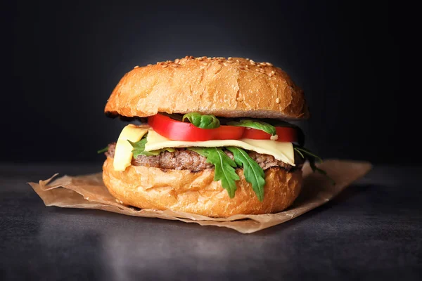 Hambúrguer saboroso na mesa contra fundo escuro — Fotografia de Stock