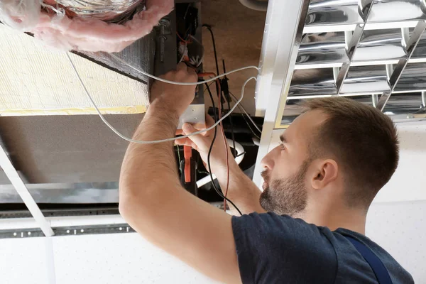 Técnico masculino que mide el voltaje durante la reparación del aire acondicionado industrial en interiores —  Fotos de Stock