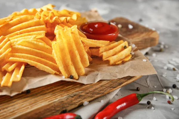 Crispy potato chips with chili pepper and sauce on wooden board, closeup — Stock Photo, Image