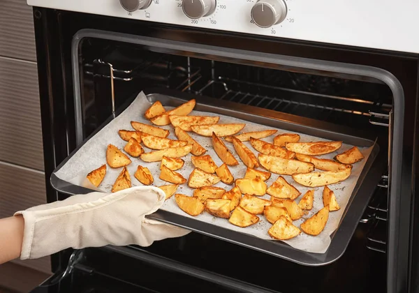 Vrouw nemen van bakplaat met heerlijke aardappelen uit de oven — Stockfoto