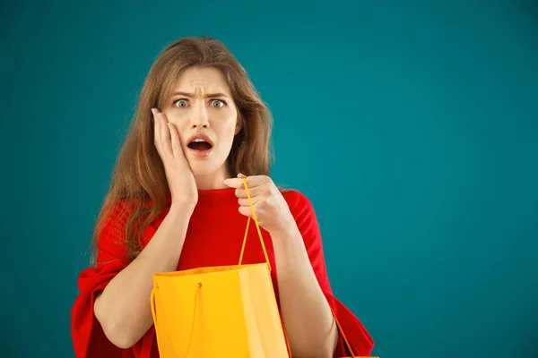Emotionele jonge vrouw met boodschappentas op kleur achtergrond — Stockfoto