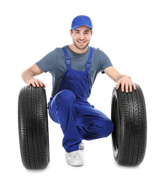 Jeune mécanicien en uniforme avec des pneus de voiture sur fond blanc — Photo