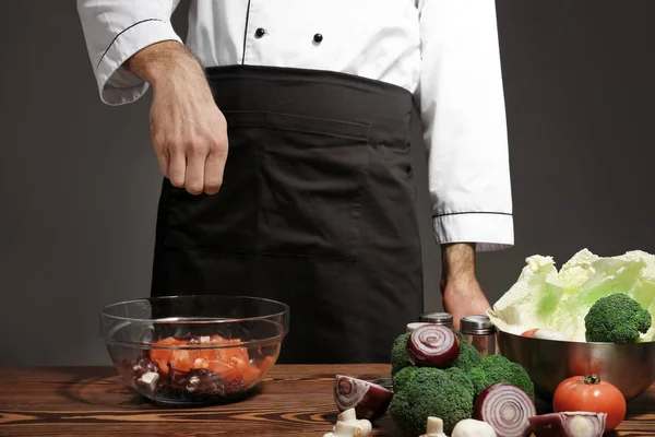 Cuoco maschio in uniforme che aggiunge spezie a gustoso piatto in tavola, primo piano — Foto Stock