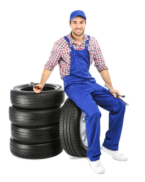 Giovane meccanico in uniforme con pneumatici auto su sfondo bianco — Foto Stock