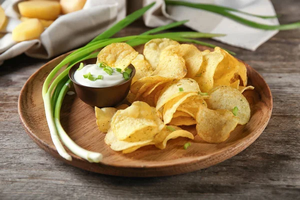 Batatas fritas crocantes com cebola verde e creme azedo em placa de madeira — Fotografia de Stock