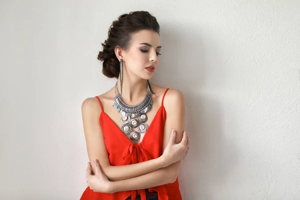 Schöne junge Frau mit elegantem Schmuck auf hellem Hintergrund — Stockfoto