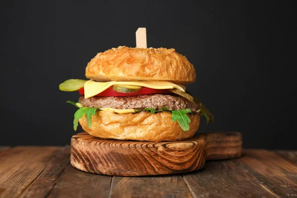 Hambúrguer saboroso na placa de madeira contra fundo escuro — Fotografia de Stock