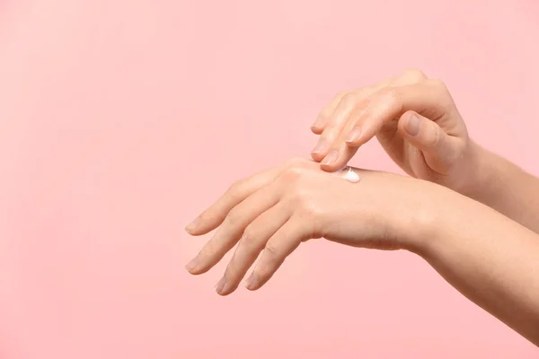 Mujer aplicando crema corporal sobre la piel sobre fondo de color — Foto de Stock